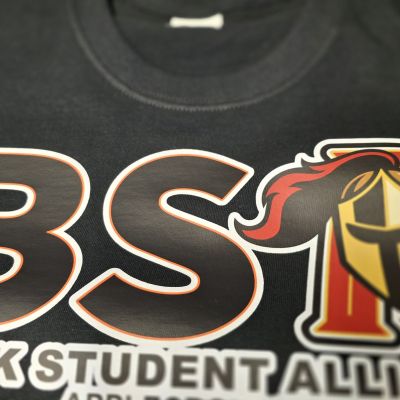 Black Student Alliance logo on a T-shirt, featuring bold letters and a shield emblem.