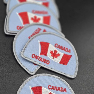 Embroidered light blue patch with waving Canadian flag, red maple leaf, and the words 