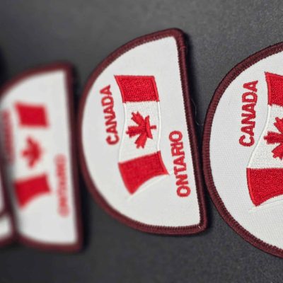 Embroidered whiteb patch with waving Canadian flag, red maple leaf, and the words 